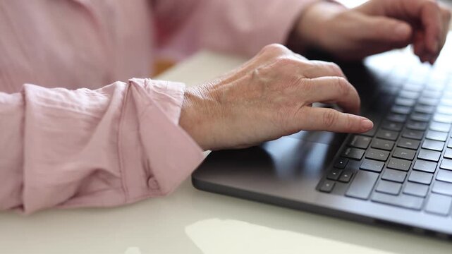 Close-up of senior woman hands using a laptop touchpad at home. Mature woman browsing the internet, working online or using digital technology.