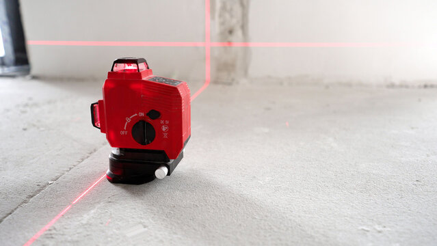 Red laser level projecting cross lines on concrete floor and wall in unfinished room