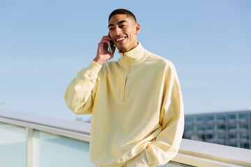 Obraz premium Young man on rooftop talking on phone in a pale yellow pullover for lifestyle background banner and website hero design