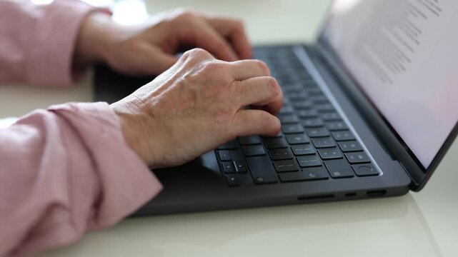 Close-up of senior woman hands typing on a laptop keyboard at home. Mature woman using a computer for online work, communication, writing or everyday digital tasks.