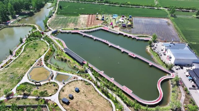 Aerial view of wetland park featuring winding waterways and red pedestrian walkways surrounded by greenery and agricultural fields