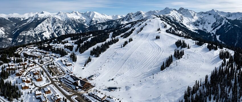 Snowy mountain range with ski resort and evergreen trees in aerial view