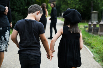 Obraz premium Two children holding hands at a park, dressed in black attire.