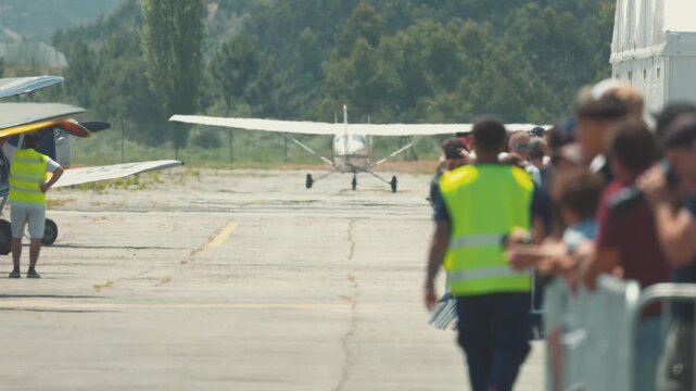 Crowd watches as small plane prepares for takeoff at airfield event in summer