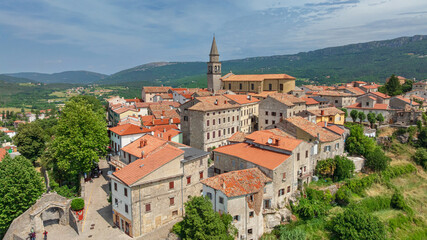 Fototapeta premium Aerial drone shot outlines historic town of Buzet situated on hill in northern Istria. Old stone buildings and modern outskirts blend with agricultural green fields and rolling countryside hills.