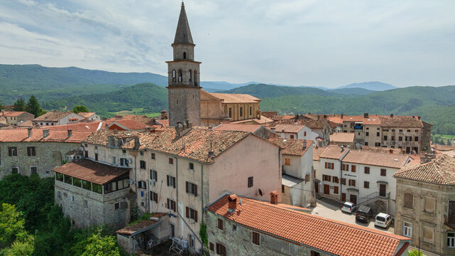 Aerial drone shot outlines historic town of Buzet situated on hill in northern Istria. Old stone buildings and modern outskirts blend with agricultural green fields and rolling countryside hills.