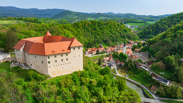 Drone captures majestic historic Celje Castle standing on green hill. Powerful stone fortification walls, towers, and inner yards look over beautiful valley during bright summer day.