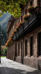 Fototapeta premium Long view of a historic building featuring a black metal balcony filled with flowers under a bright sky and lush green leaves
