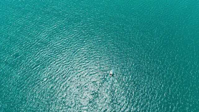 A small boat moves slowly across the smooth ocean water. The sun reflects off the surface, creating bright spots. This scene shows a clear day at sea.