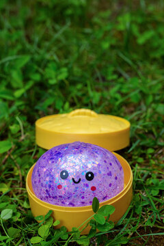 Purple glitter kawaii squishy dumpling toy in open yellow plastic steamer container on green grass