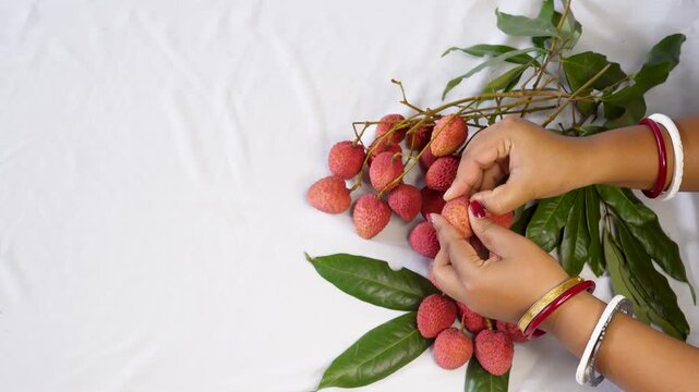 A woman hand Holding a Freshly Peeled Lychee Fruit, Revealing Its Juicy White Flesh and red Outer Shell on keep black bowl. inside with another whole lychee or litchi fruits.