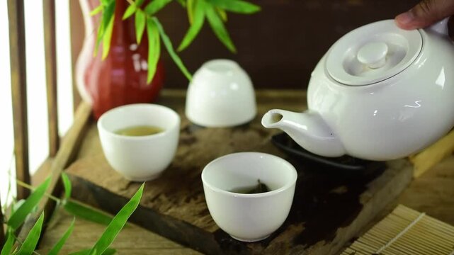 Slow motion video of pouring hot Chinese oolong tea from a white ceramic teapot into a cup. Serene Zen atmosphere with bamboo leaves, perfect for traditional Asian culture and relaxation.