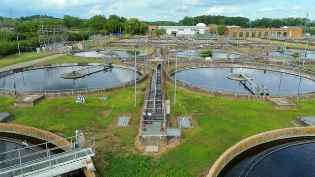 Close-up aerial view of a huge sewage wastewater treatment plant with circular clarifiers and active aeration ponds in Hoddesdon, UK.