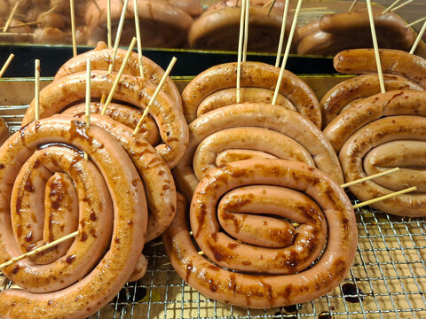 Multiple spiral-coiled sausages on wooden skewers arranged on a metal cooling rack