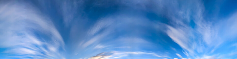 Obraz premium Panorama blue sky with white fluffy clouds. Copy space on panorama of some long cirrus arc clouds drifting calmly across the sky toward the viewer. A majestic spectacle of nature's elements.
