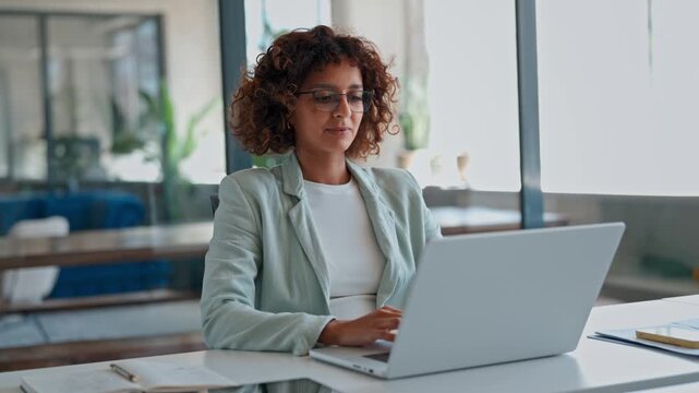 Indian or muslim arabian businesswoman working on laptop at modern office desk. Professional woman ceo entrepreneur using pc computer for online finance management or marketing sitting at workplace.