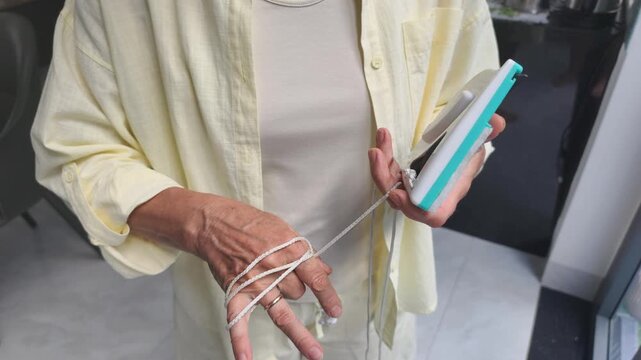 Woman secures cleaning tool by wrapping cord on hand. Reliable protection measures keep cleaning tool safe from sudden high fall, making magnetic window washing process calm and completely risk-free.
