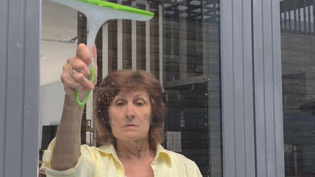 Woman puts ultimate finish touch to window washing routine using green squeegee. Perfect finish touch helps female worker instantly clear away water drops, leaving glass immaculate and shiny.