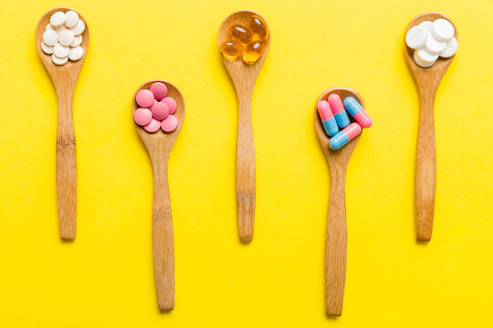 Vitamin capsules in a spoon on a colored background. Pills served as a healthy meal. Red soft gel vitamin supplement capsules on spoon