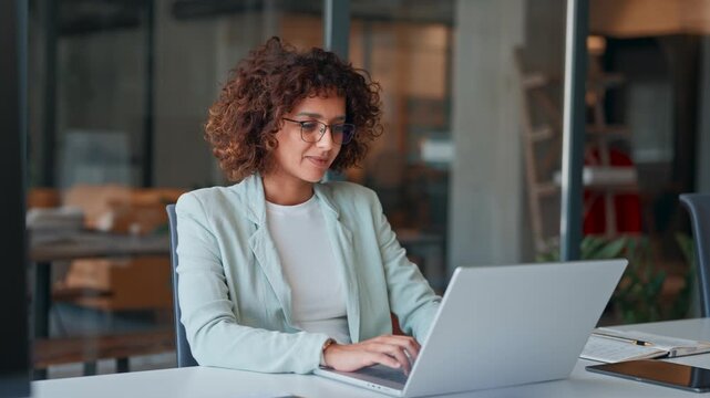 Young professional specialist latin hispanic businesswoman in suit working on laptop pc sitting at desk in office. Middle eastern indian woman using computer technology app for work online. Copy space