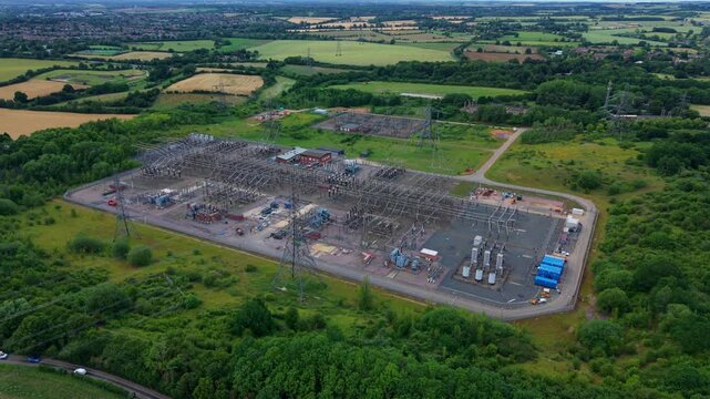 High angle drone view of a national grid electricity substation featuring transmission busbars, transformers, and switchyard equipment.