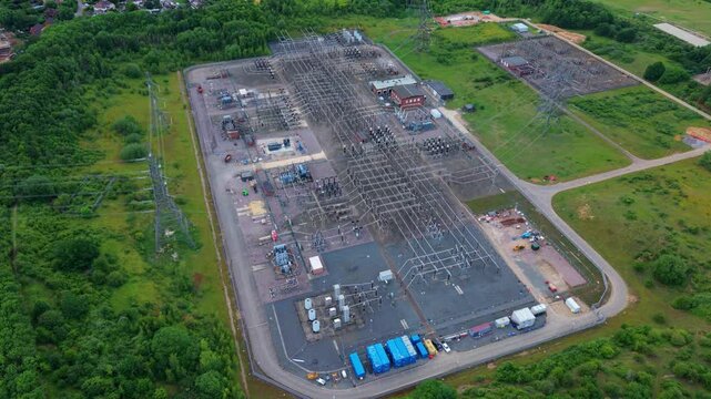 High angle drone view of a national grid electricity substation featuring transmission busbars, transformers, and switchyard equipment.