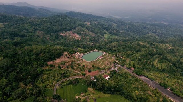 Aerial drone footage of Embung Nglanggeran, a scenic artificial reservoir located in the Ancient Nglanggeran Volcano area, Yogyakarta, Indonesia.