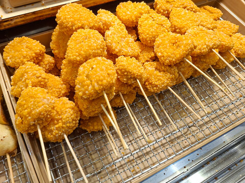 Rows of deep-fried, golden-yellow skewered nuggets or fish cakes resting on a metal mesh tray