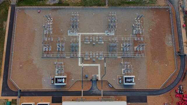Aerial view of a massive electrical substation with switchgear units, busbars, and high-voltage power lines in Biggleswade, UK.