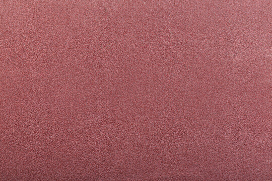 Red abrasive sandpaper belt texture with dense grit and rough uneven surface detail