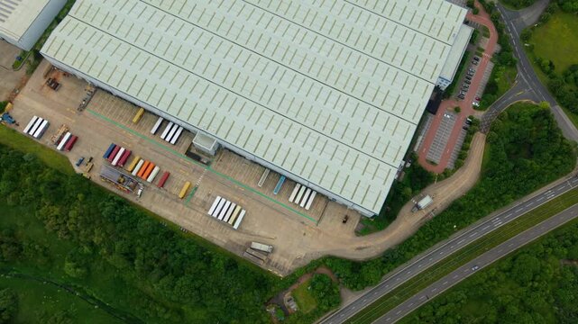 Top down aerial view of a large commercial distribution centre warehouse with rows of HGV lorries parked in loading bays.