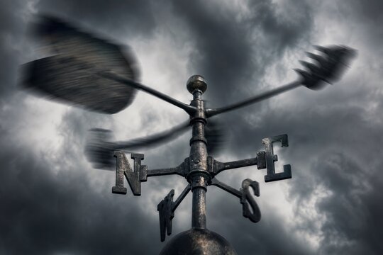 Close-up of a weather vane spinning rapidly against dark turbulent storm clouds, motion blur.