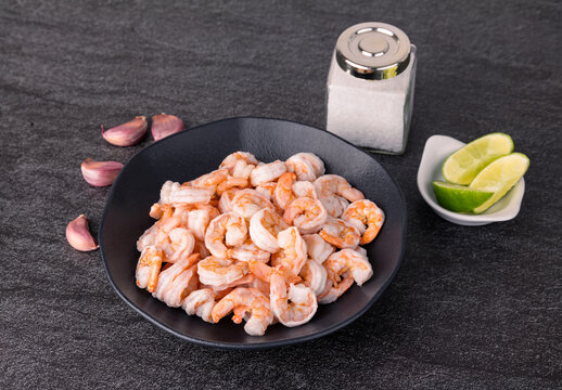 Uncooked orange shrimps in a black plate over stone background