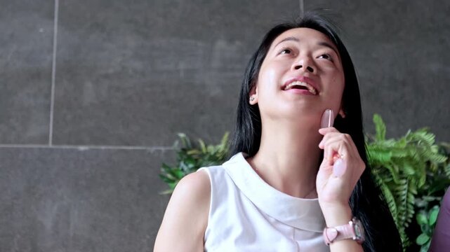 Young Asian woman massaging her face with a gua sha stone