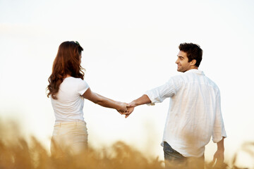 Obraz premium Couple, holding hands and walking outdoor in meadow, partner and support with care in nature. People, marriage and romantic stroll for healthy relationship, bonding and together with space for love