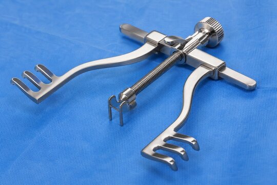 A stainless steel tissue retractor on a blue surgical drape under bright lights.