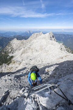 Hiker in a secured path, climbing a ladder, ascent to the Mitterhorn, steep rocky mountain landscape, in the background rocky ridge with peaks Gro&szlig;es Rothorn and &Ouml;stliches Rothorn, Nuaracher H&ouml;henweg, Loferer Steinberge, Tyrol, Austria