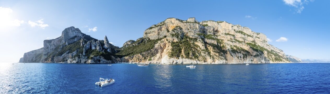 Motor boat off picturesque rocky coast, cliffs with L'Aguglia pinnacle, blue sea and Cala Goloritz&eacute; beach, aerial view, Golfo di Orosei, Baunei, Sardinia, Italy
