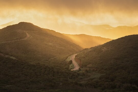 View from a path below the summit of Garajonay to other mountains of the Garajonay National Park and a road. After a rain shower, with sun and golden hour with bright clouds. Parque Nacional de Garajonay, La Gomera, Canary Islands, Spain