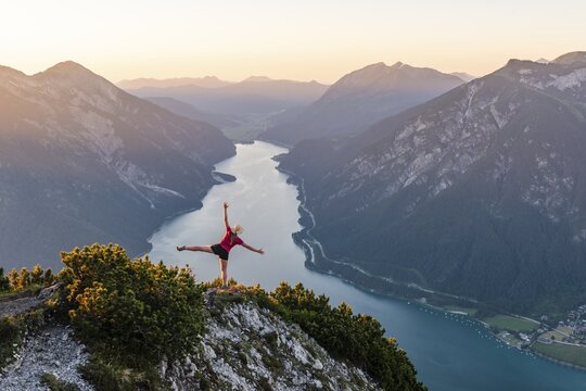 Sunset, young woman stretches arms in the air, view from the mountain B&auml;renkopf to Lake Achensee, left Seebergspitze and Seekarspitze, right Rofan Mountains, Tyrol, Austria