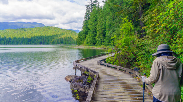 Senior female hiking on lakeside boardwalk on Sasamat Loop trail in Belcarra Provincial Park, BC, Canada.