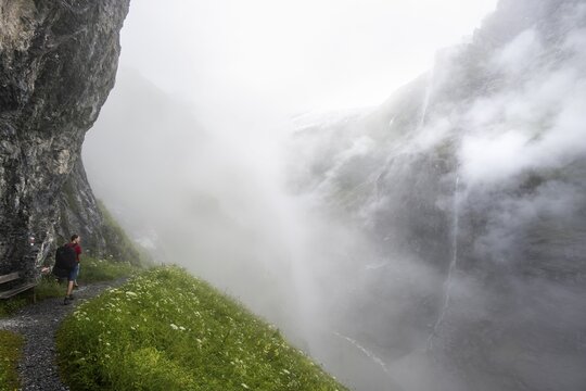 Mountaineer hiking on a hiking trail on a steep rock face, hiking to Berghaus B&auml;regg, cloud-covered rock gorge with waterfall, Bernese Alps, Bernese Oberland, Switzerland