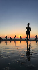 Fototapeta premium Yoga group practices mindfulness and physical exercise during a golden hour sunset on the reflective sandy beach shore.