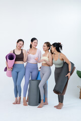 Fototapeta premium Asian female friends laugh together with yoga mats, sharing cheerful class moment, wellness motivation, friendship support, fitness progress, healthy lifestyle energy on clean studio backdrop.