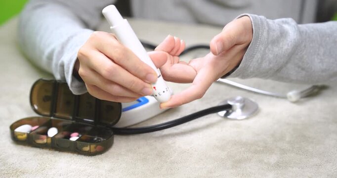 Close-up of a person performing a fingertip blood glucose test using a lancing device at home. Self health monitoring, diabetes management, wellness tracking, preventive care, and healthy lifestyle co