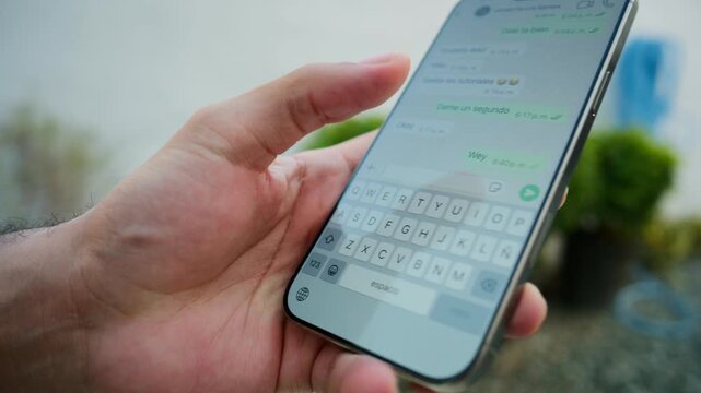 Close up view of a man's hand typing a text message on a smartphone keyboard outdoors
