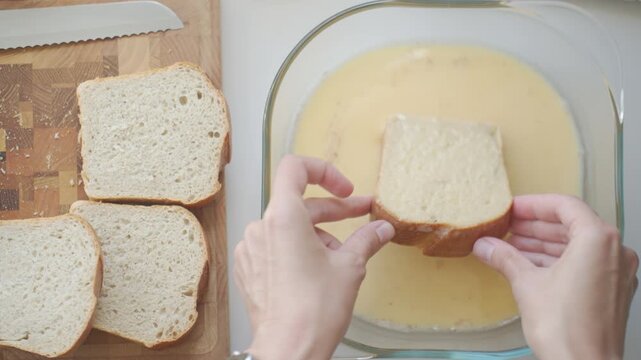 Bread dipped in egg mixture in glass dish, with more slices on a cutting board nearby. Concept of breakfast recipe and simple cooking