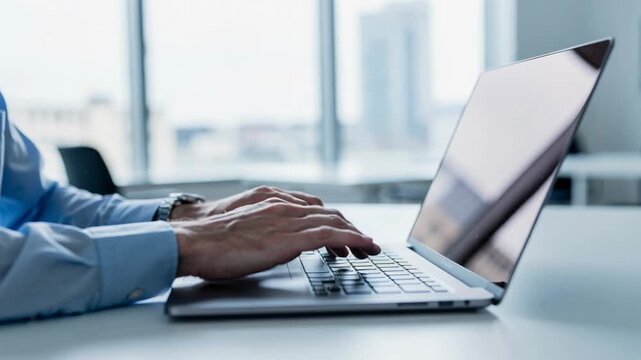 Businessman typing on laptop computer in modern office with city view during work