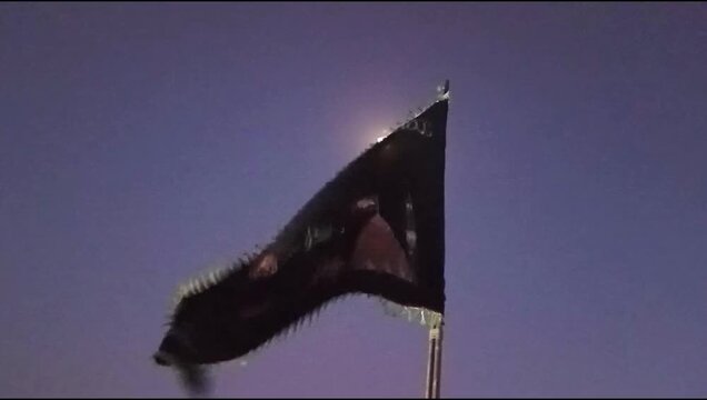 Black Alam Flag with Silver Symbols During Muharram Commemoration Against Evening Sky