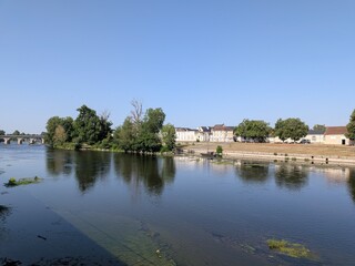 Fototapeta premium Scenic view of the Vienne river in Chatellerault with the historic Henri IV stone bridge and a traditional boat moored near the island, France.
